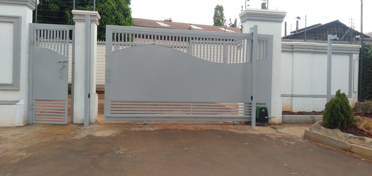Grey steel sliding gate with rack and green motor beside a matching pedestrian gate