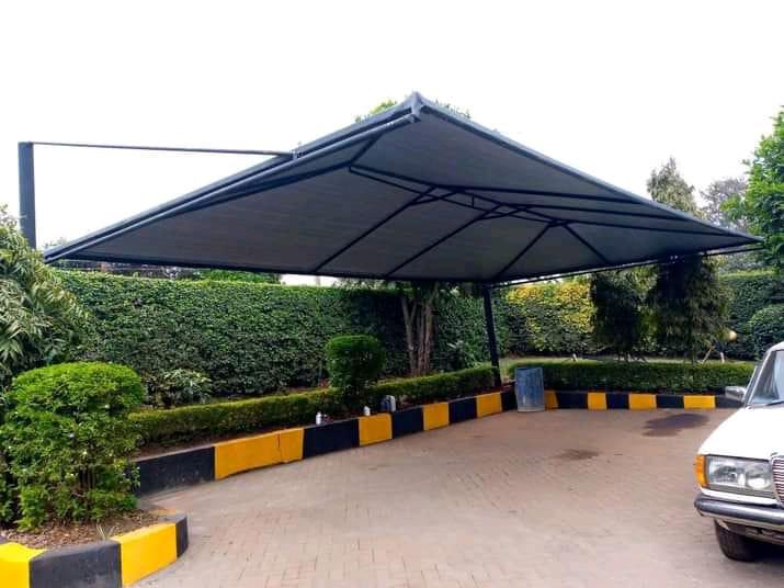 Dark shade net cantilever carport over a paved parking bay with hedges