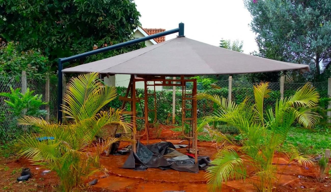 Large cantilever umbrella with a brown canopy on a steel arm being installed in a garden