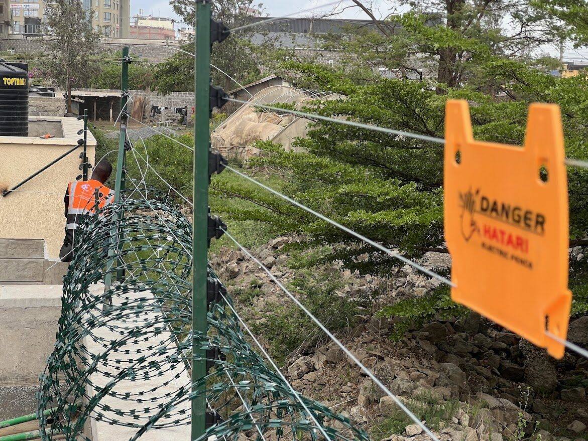 Electric fence with razor wire coils along a perimeter, with a technician at work