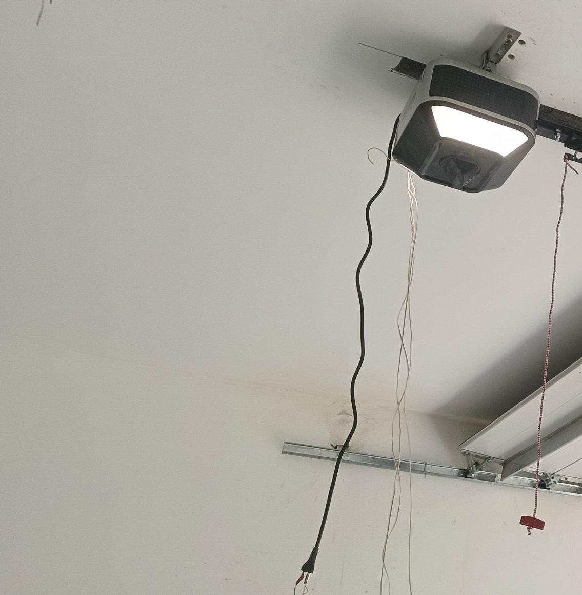 Ceiling-mounted garage door opener motor with rail and arm above sectional door panels