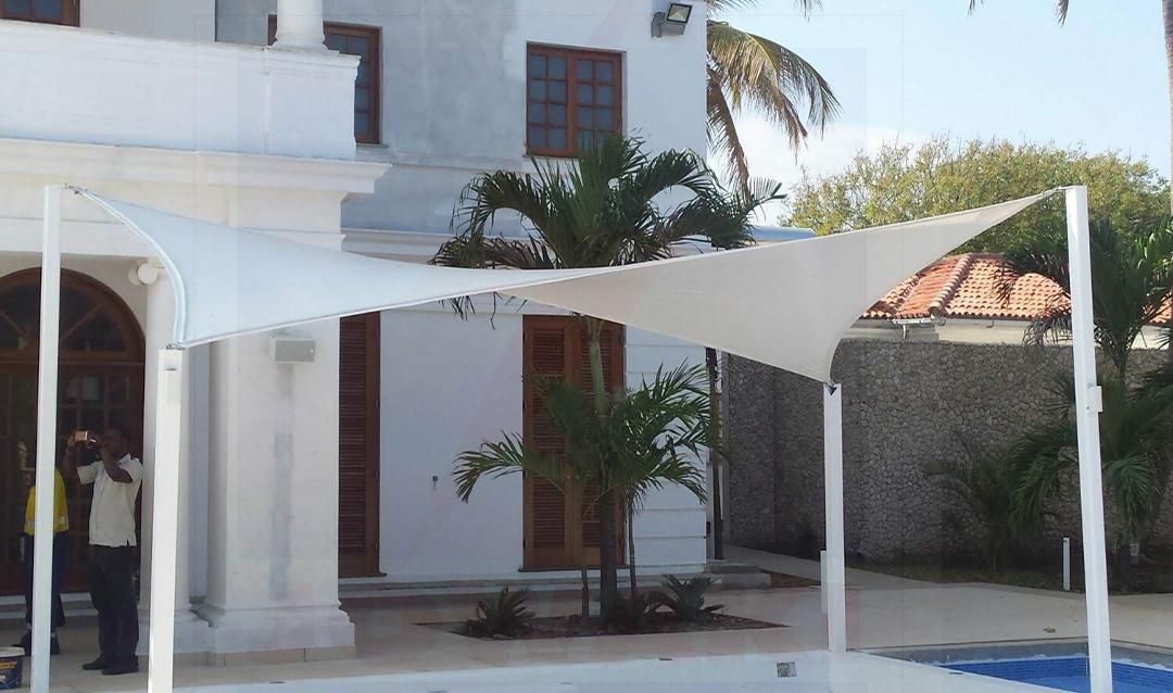 White triangular shade sail on steel poles over a patio beside a pool