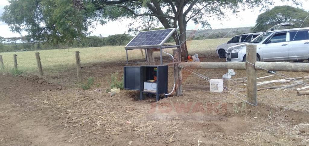 Electric fence energiser with a solar panel and battery box on a farm boundary