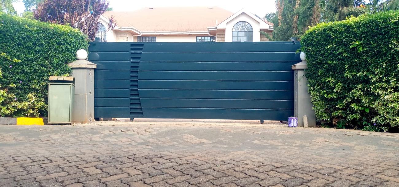 Dark green horizontal-panel sliding gate between stone gate pillars
