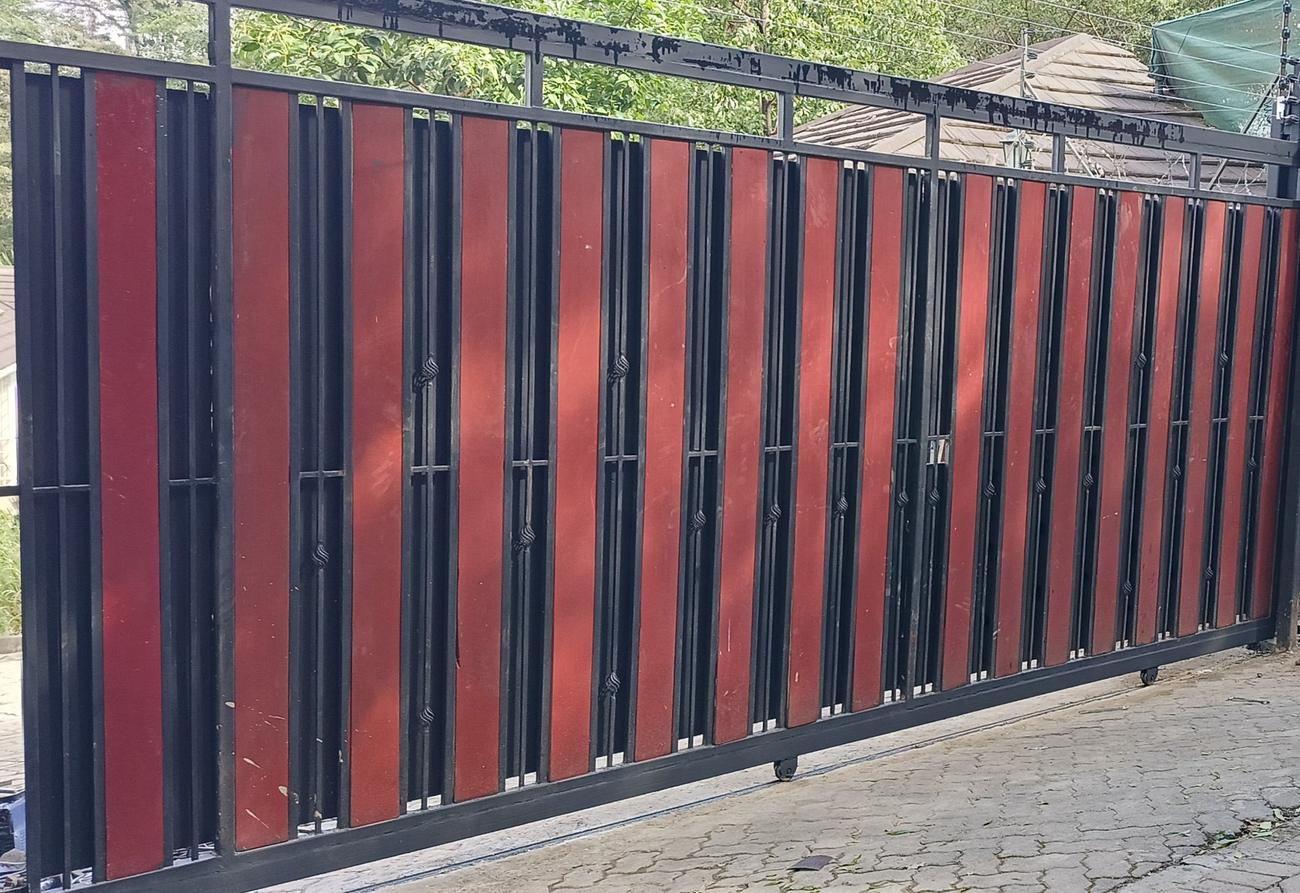 Black steel sliding gate with red vertical panels on a cobbled driveway