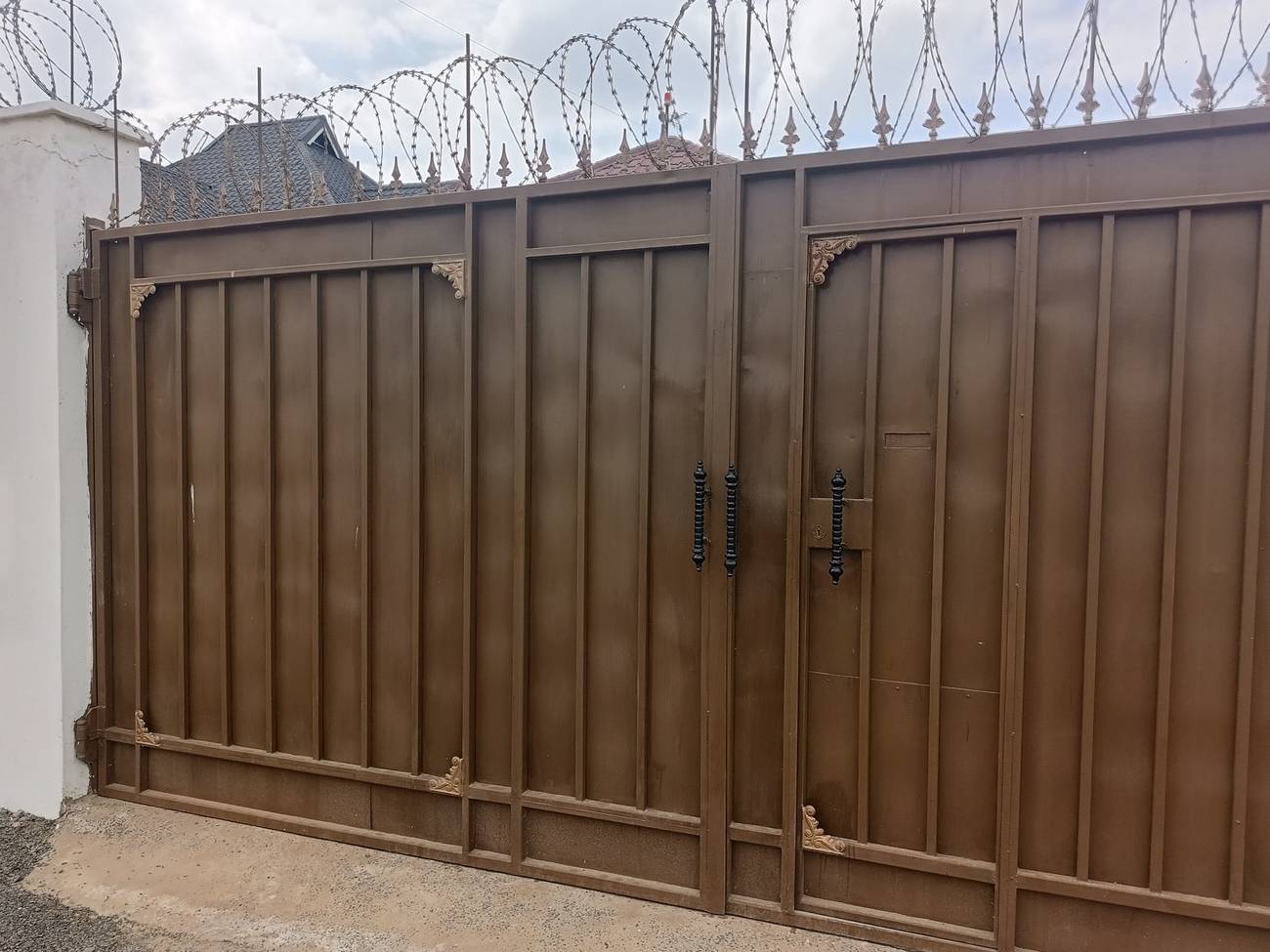 Brown steel swing gate with decorative corners and razor wire on top