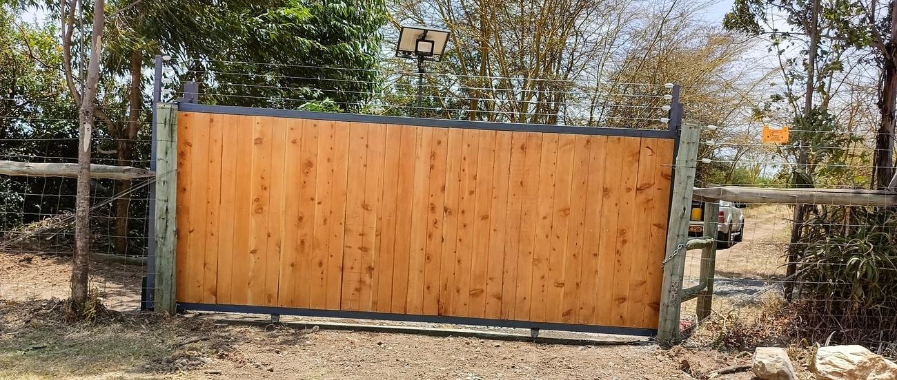 Timber-clad sliding gate with electric fence strands and a solar floodlight